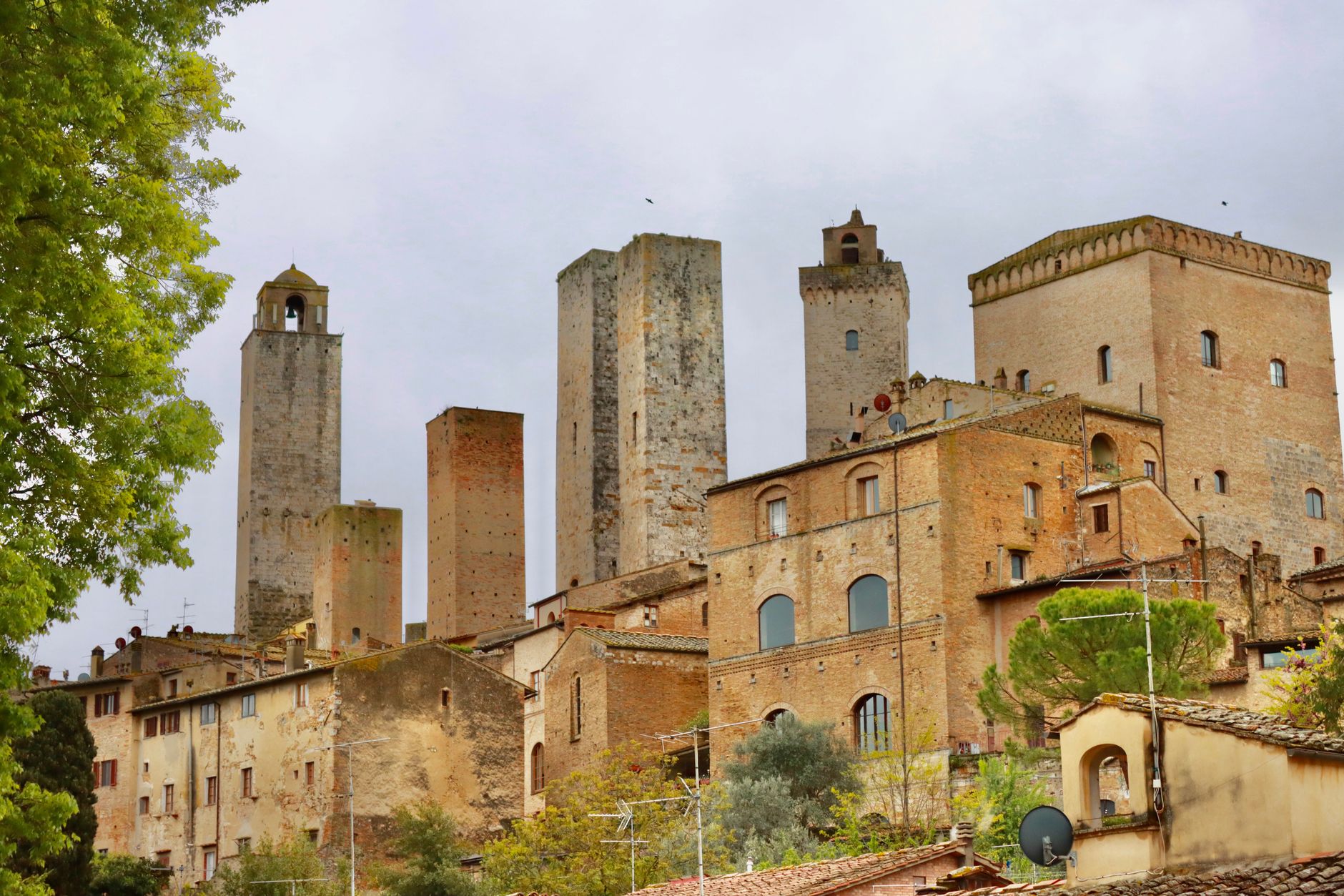 Středověké věže městečka San Gimignano nad střechami a toskánskou krajinou