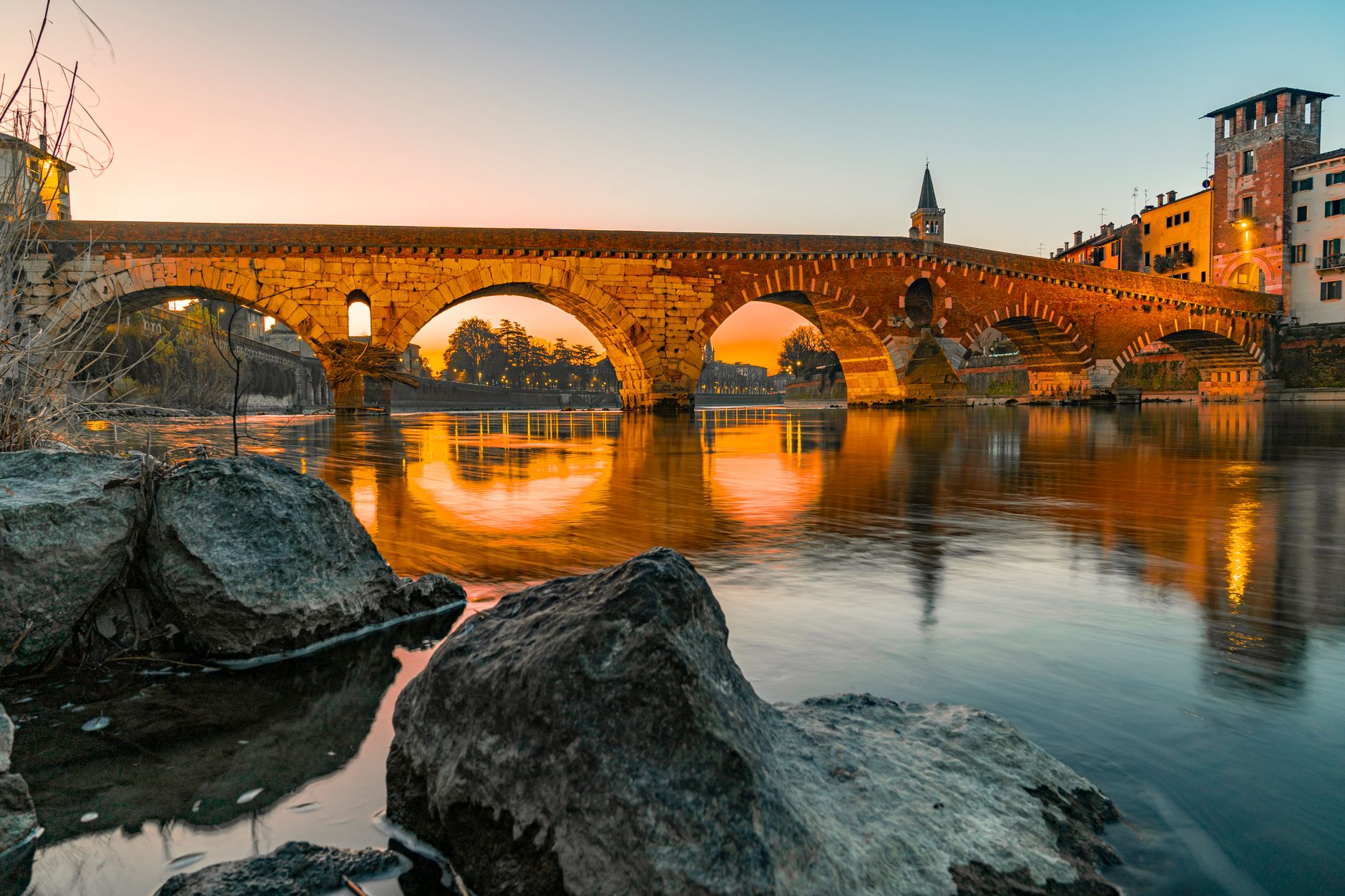 Pohled na řeku Adiže ve Veroně s kamenným mostem Ponte Pietra a věžemi v pozadí