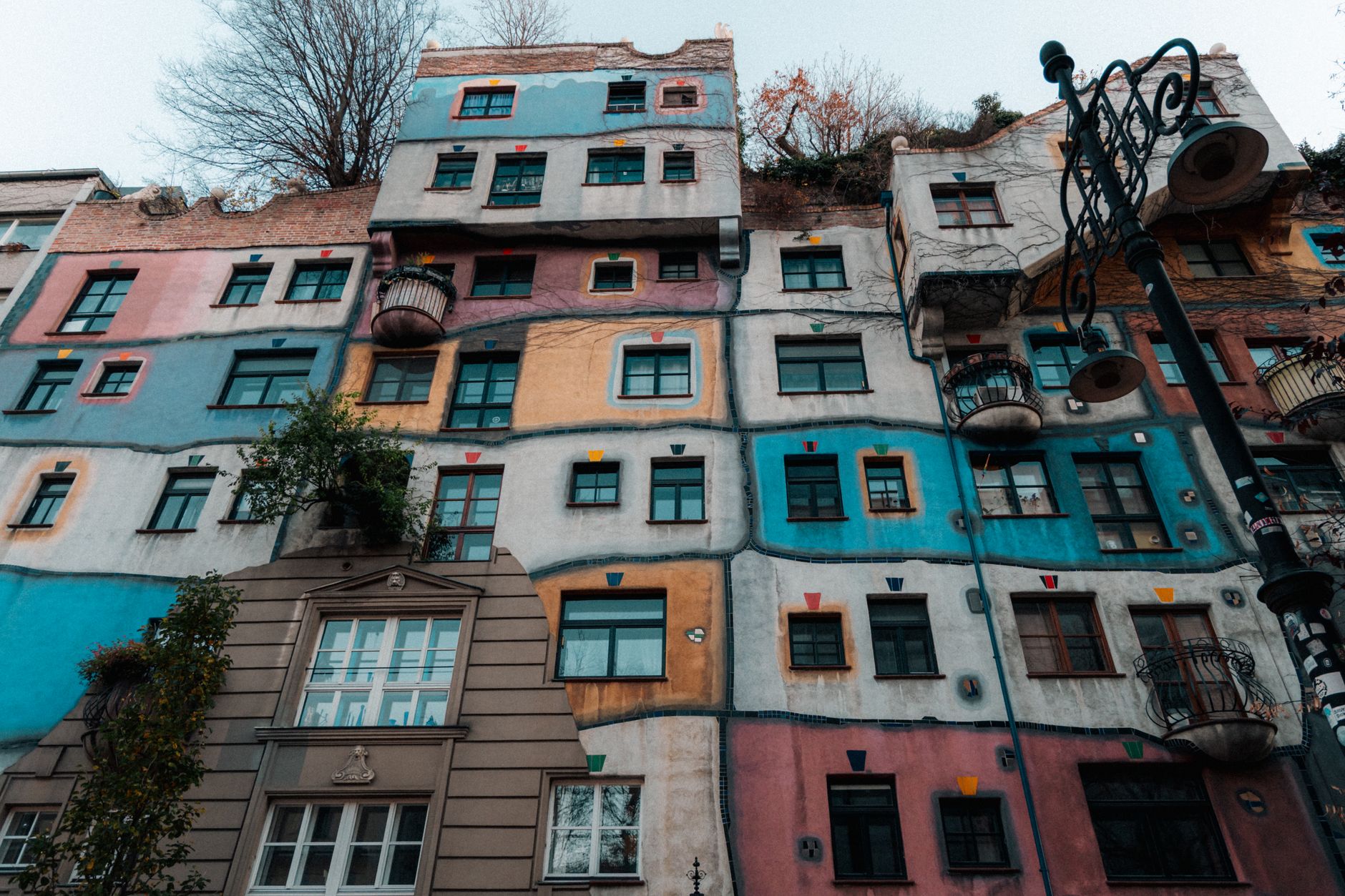 Pestrobarevná fasáda domu Hundertwasserhaus ve Vídni s nepravidelnými okny a zelení