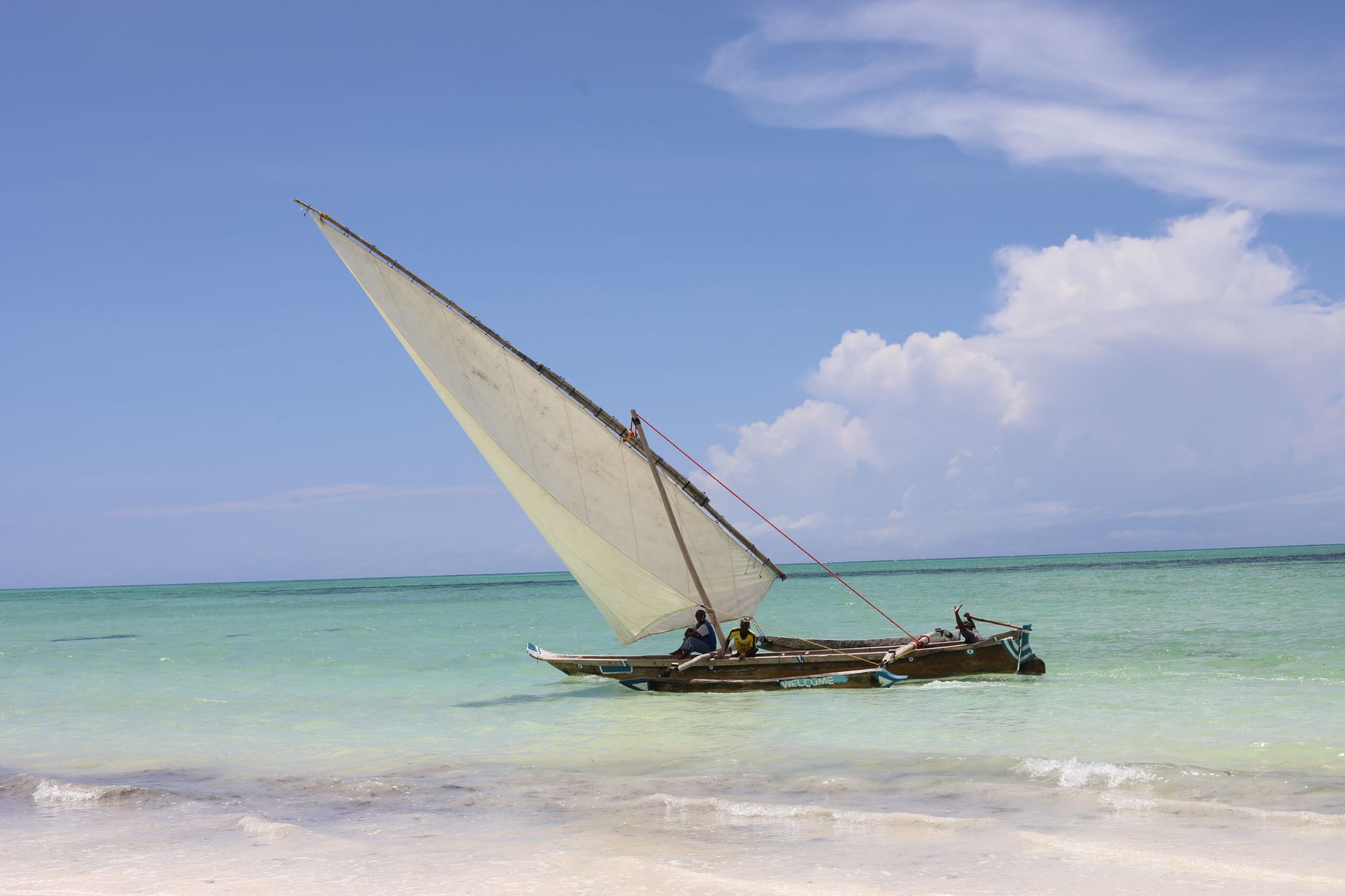 Bílá pláž na Zanzibaru s tyrkysovým mořem a tradiční dřevěnou plachetnicí dhow při odlivu