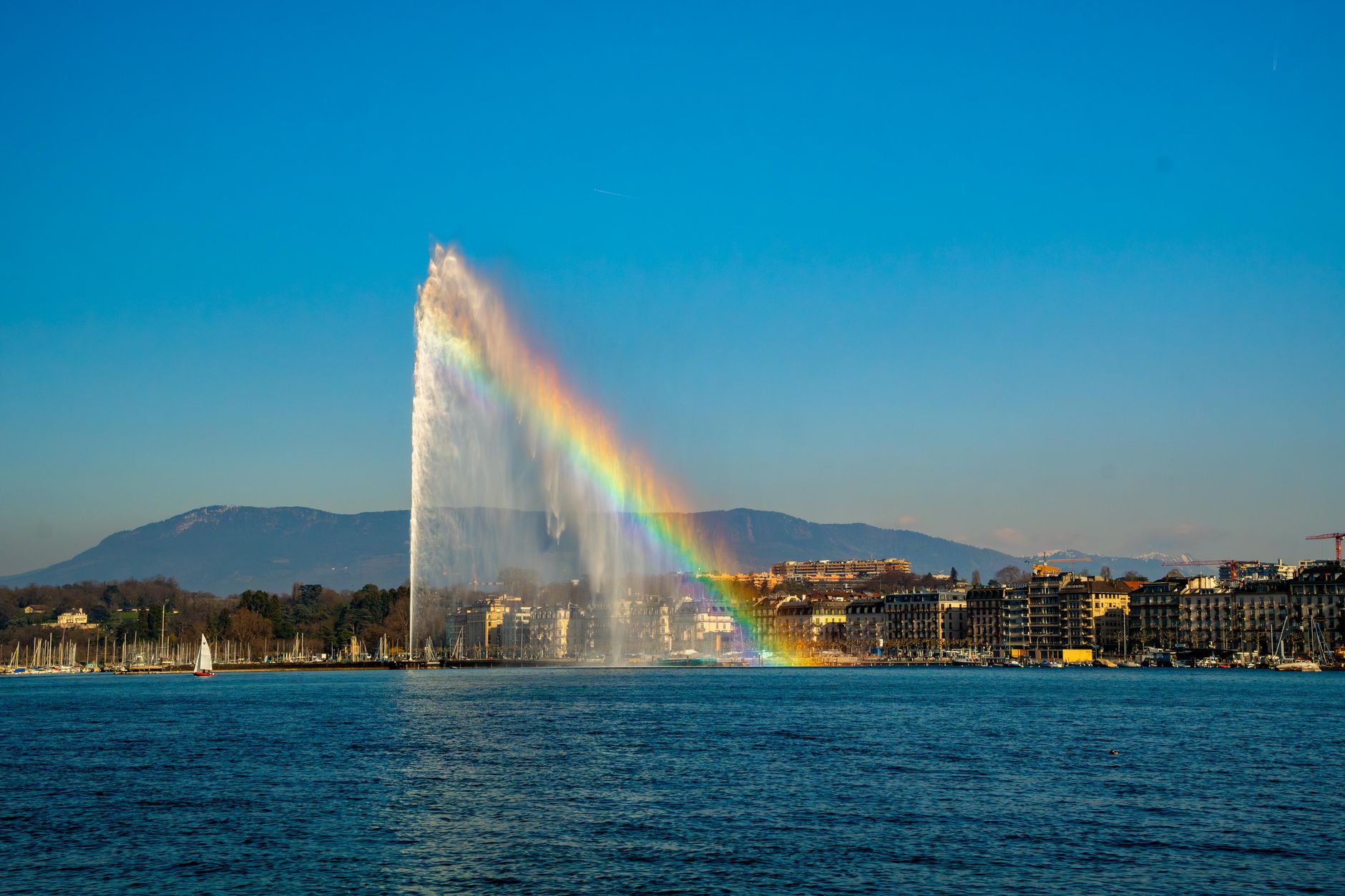 Vodotrysk Jet d'Eau na Ženevském jezeře s panoramatem města a Alpami v pozadí