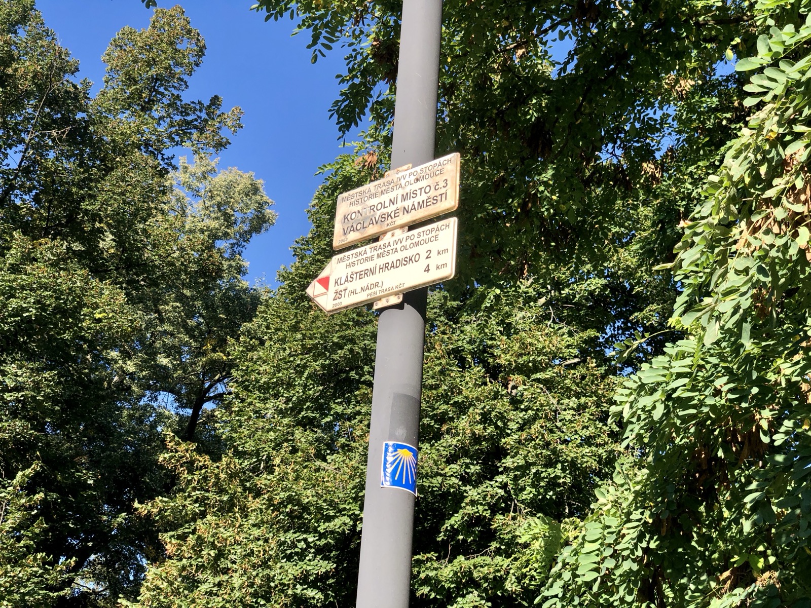Turistický rozcestník na moravské trase s modrobílou cedulkou s mušlí svatého Jakuba na sloupku