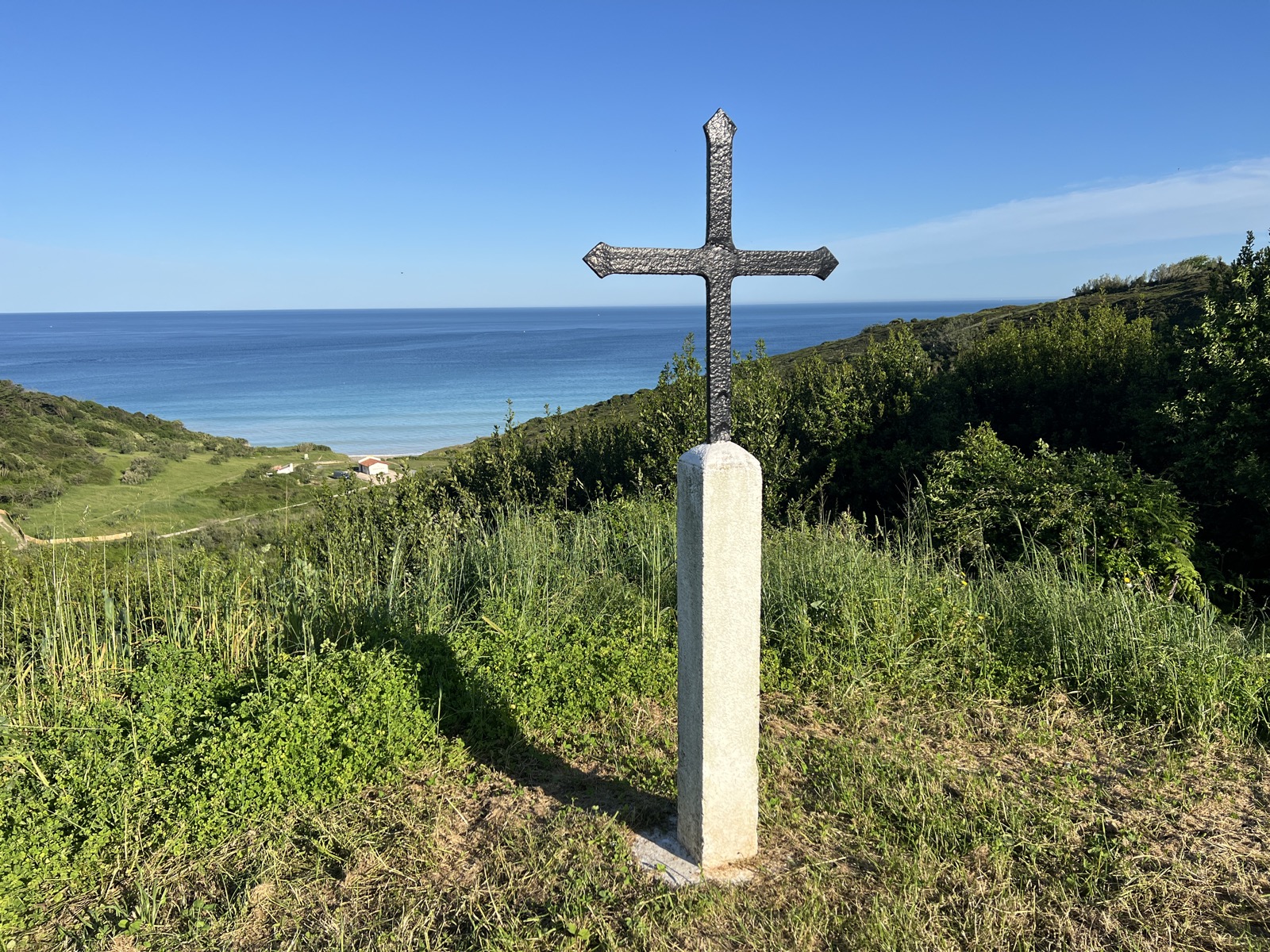 Kamenný kříž na kopci nad pláží a oceánem na Camino del Norte